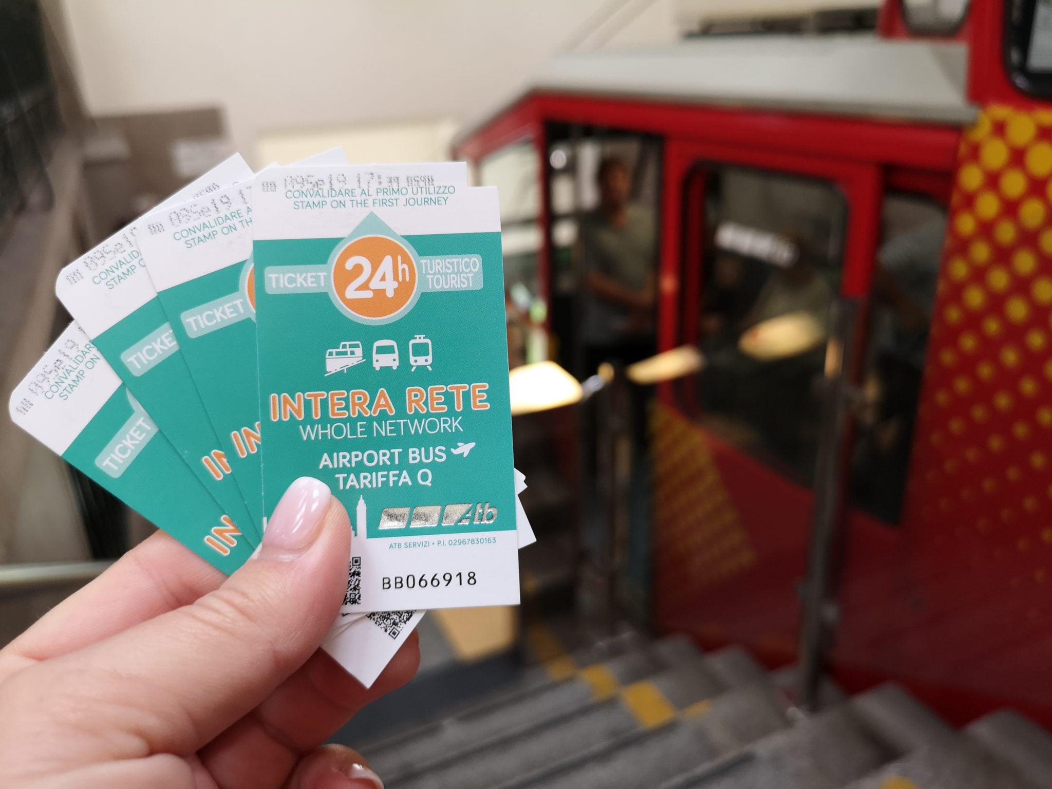 Osoba trzymająca w dłoni bilety na kolejkę w Bergamo, w tle czerwony wagonik kolejki