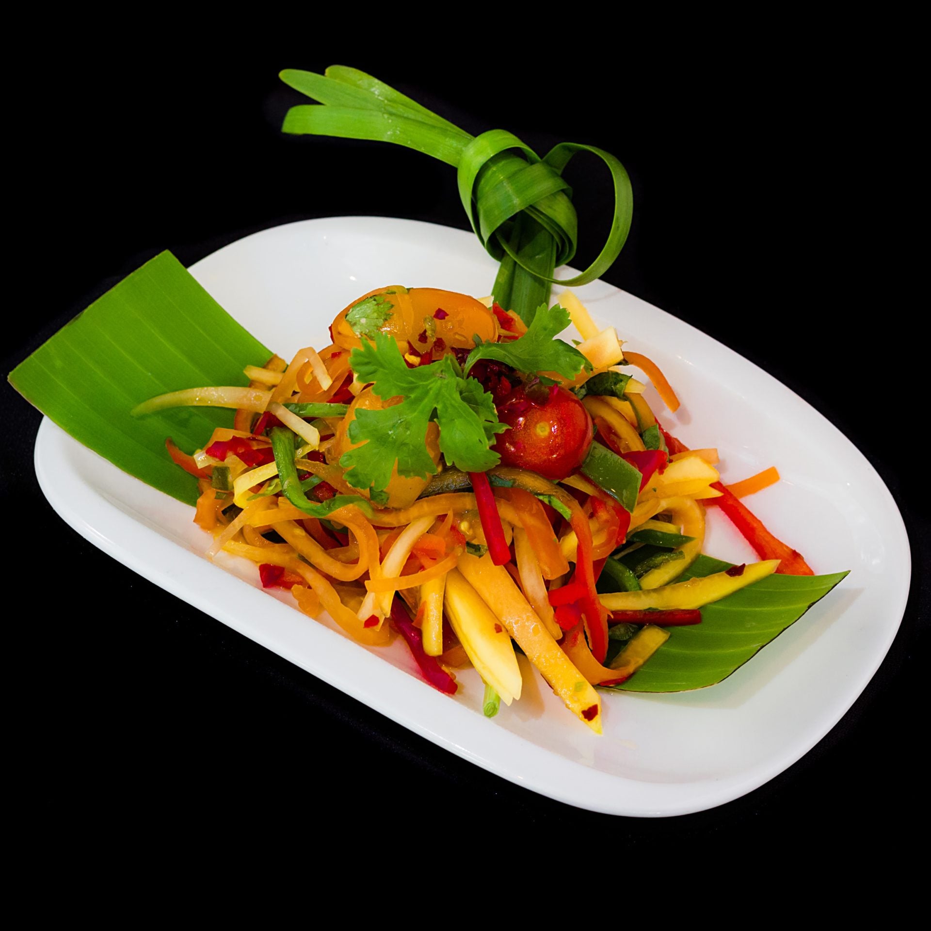 na talerzyku sałatka z zielonej papai, z czosnkiem, chilli, fasolką zieloną i pomidorkami koktajlowymi