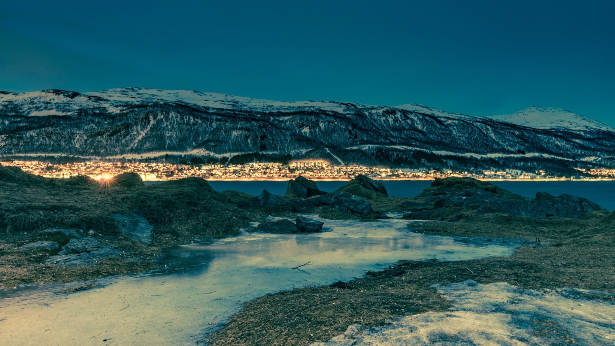 Panorama na miasteczko Tromso, otaczające je zaśnieżone fiordy i morze nocą