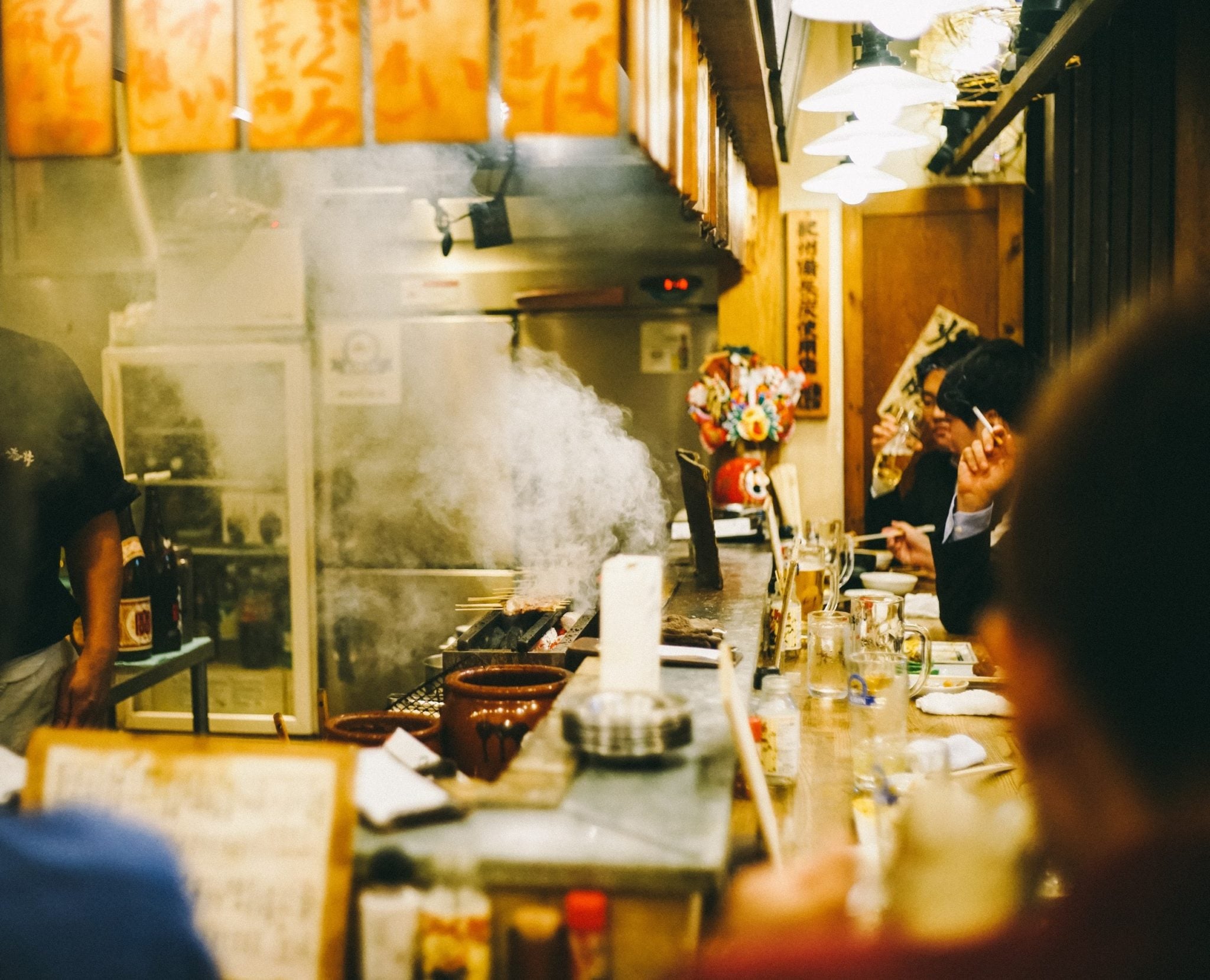 Ludzie siedzący przy ladzie w japońskiej restauracji w centrum Tokio, z garnków bucha para, ludzie czekają na podanie jedzenia